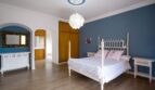 Helles Schlafzimmer der Villa in Marratxí mit blauer Akzentwand, weißem Himmelbett und Holzboden.