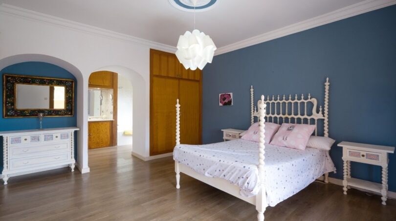 Helles Schlafzimmer der Villa in Marratxí mit blauer Akzentwand, weißem Himmelbett und Holzboden.