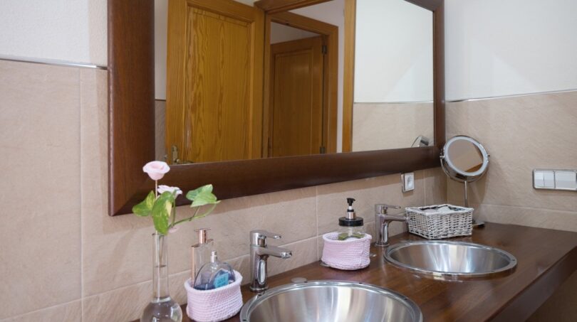 Badezimmer der Villa in Marratxí mit Doppelwaschbecken aus Edelstahl, Holzablage und großem Wandspiegel.