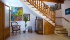 Eingangsbereich der Villa in Marratxí mit Holztreppe, Terrakottaboden, Kunstwerken und elegantem Vintage-Mobiliar.