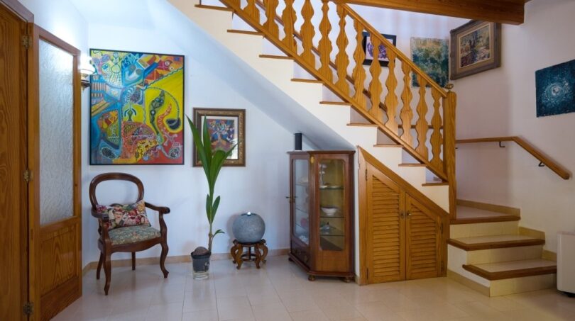 Eingangsbereich der Villa in Marratxí mit Holztreppe, Terrakottaboden, Kunstwerken und elegantem Vintage-Mobiliar.