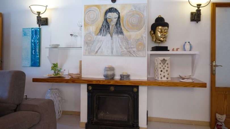Wohnzimmer der Villa in Marratxí mit Kamin, Holzregal, Buddha-Skulptur und dekorativer Wandmalerei.