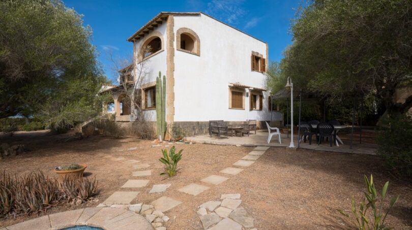 Außenansicht der Villa in Marratxí mit Pool, Steinweg, Terrasse und mediterranem Baumbestand unter blauem Himmel.
