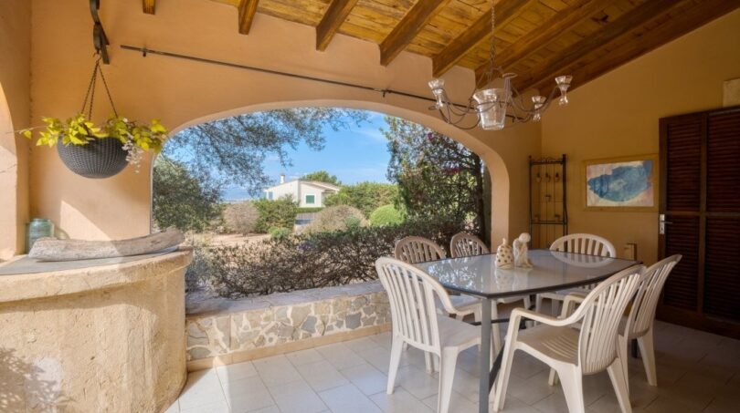 Überdachte Terrasse der Villa in Marratxí mit Holzbalkendecke, Esstisch und Blick ins Grüne.
