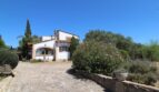 Außenansicht Villa Marratxí: weißes Landhaus mit Rundbogenfenster, Natursteineinfahrt und mediterranem Garten bei blauem Himmel.