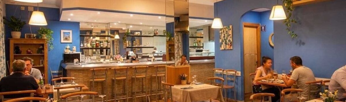 Restaurante mediterráneo con paredes azules, lámparas colgantes, bar e iluminación acogedora en Palma de Mallorca.