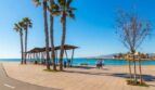 Strandpromenade in Palma de Mallorca mit Palmen, Holzpavillon und türkisblauem Mittelmeer