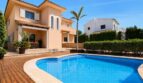 Vista exterior de la villa en Llucmajor con gran piscina, terraza de madera, palmera y fachada mediterránea