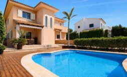 Vista exterior de la villa en Llucmajor con gran piscina, terraza de madera, palmera y fachada mediterránea