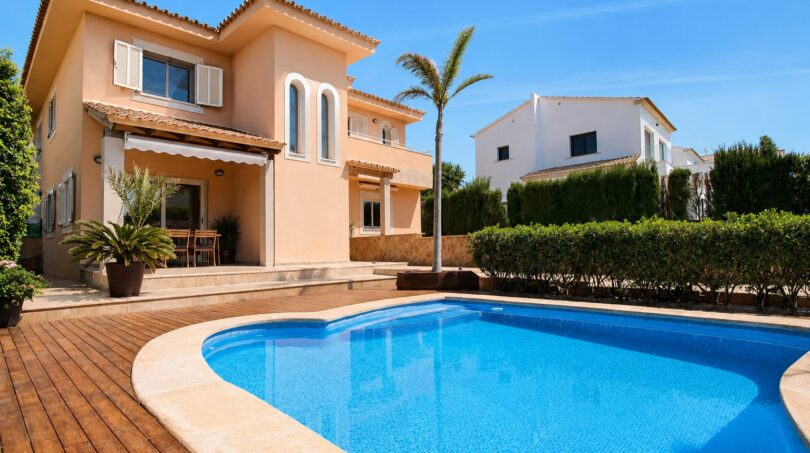 Vista exterior de la villa en Llucmajor con gran piscina, terraza de madera, palmera y fachada mediterránea
