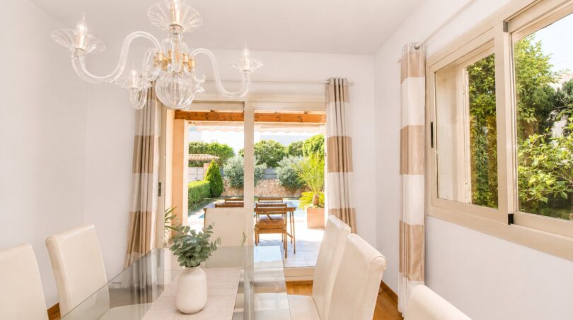 Comedor inundado de luz de la villa en Llucmajor con mesa de cristal, lámpara de araña y acceso al jardín.