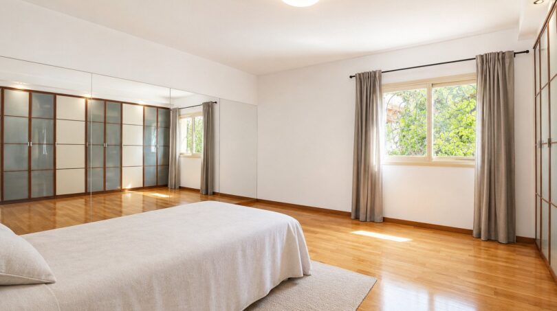 Dormitorio luminoso de la villa en Llucmajor con suelo de parquet, espejo empotrado y gran ventana con vista al jardín
