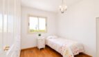Dormitorio luminoso de la villa en Llucmajor con cama individual, suelo de madera, lámpara de araña y ventana con vista al jardín.