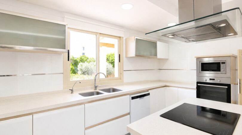 Moderna cocina blanca de la villa en Llucmajor con isla de cocción, electrodomésticos integrados y ventana hacia el jardín