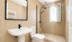 Cuarto de baño moderno de la villa en Llucmajor con azulejos beige, grifería negra, ducha tipo lluvia y ventana de arco.