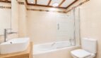 Cuarto de baño luminoso de la villa en Llucmajor con bañera, separación de cristal, lavamanos moderno y detalles de madera.