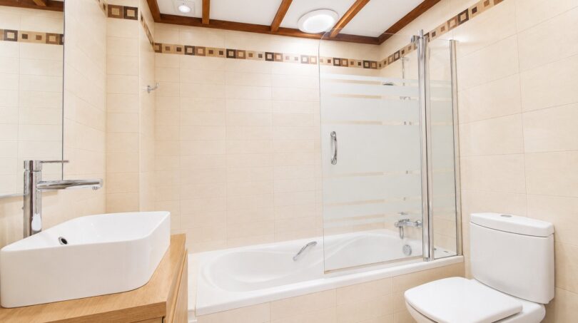 Cuarto de baño luminoso de la villa en Llucmajor con bañera, separación de cristal, lavamanos moderno y detalles de madera.