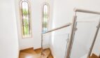 Escalera de la villa en Llucmajor con peldaños de madera, barandilla de cristal y ventanas de arco emplomado