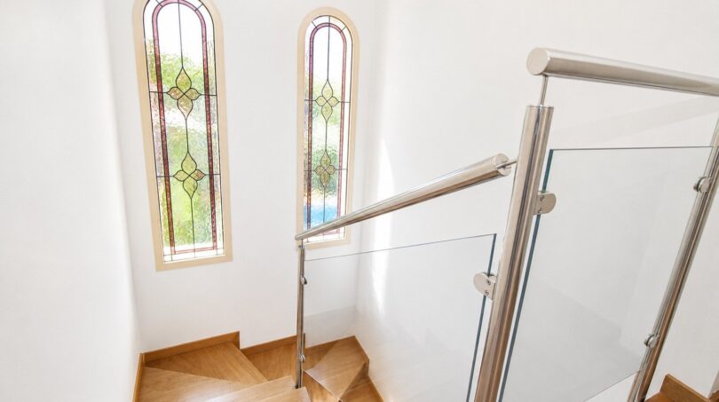 Escalera de la villa en Llucmajor con peldaños de madera, barandilla de cristal y ventanas de arco emplomado