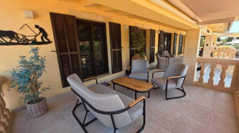 Überdachte Terrasse der Finca S'Illot mit modernen Loungesessel, Holztisch und braunen Fensterläden