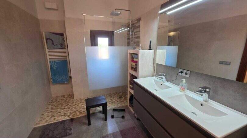 Modernes Badezimmer der Finca S'Illot mit Doppelwaschbecken, begehbarer Dusche und Naturstein-Boden.