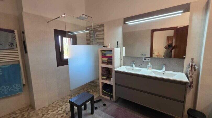 Modernes Badezimmer der Finca S'Illot mit Doppelwaschbecken, begehbarer Dusche und Holzbalkendecke.