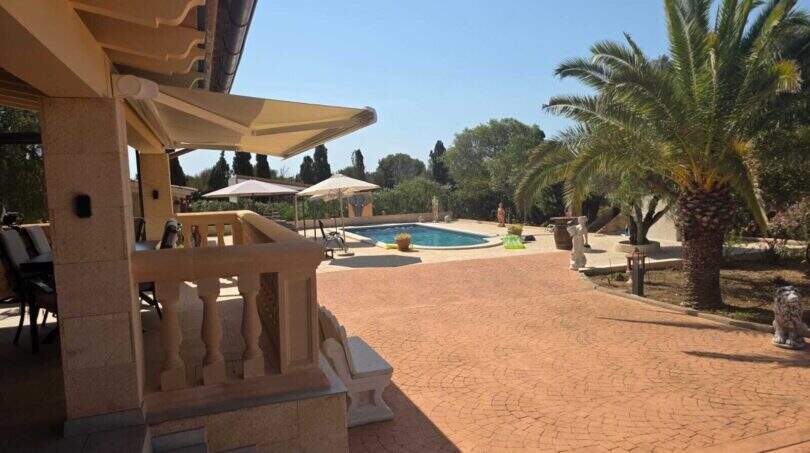 Finca S'Illot: Terrasse mit Balustrade, Markise, Pool und Palmen im mediterranen Garten