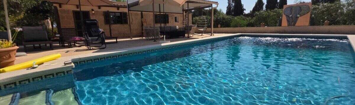 Finca S'Illot: Großer blauer Pool mit Sonnenterrasse, Pergola und mediterranem Garten im Hintergrund.