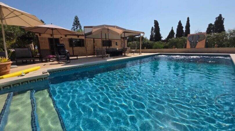 Finca S'Illot: Großer blauer Pool mit Sonnenterrasse, Pergola und mediterranem Garten im Hintergrund.