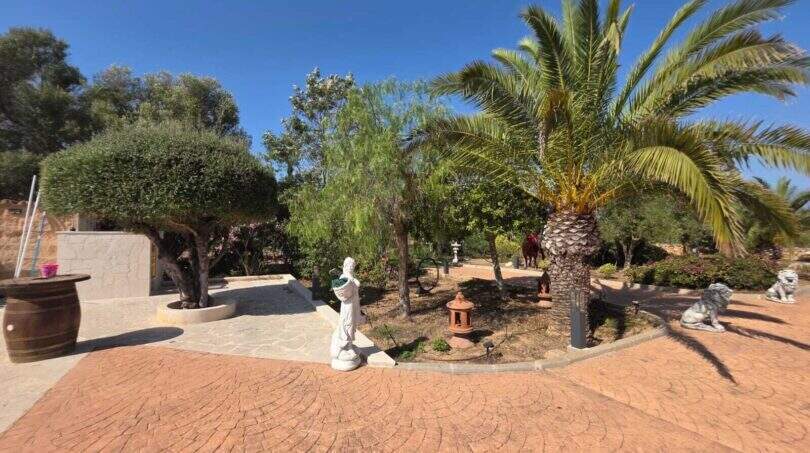 Mediterraner Garten der Finca S'Illot mit Palmen, Skulpturen, Löwenstatuen und gepflastertem Vorplatz.
