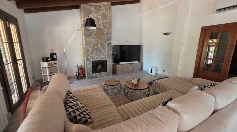 Wohnzimmer der Finca S'Illot mit Steinofen, Holzbalkendecke, großem Sofa und TV-Bereich