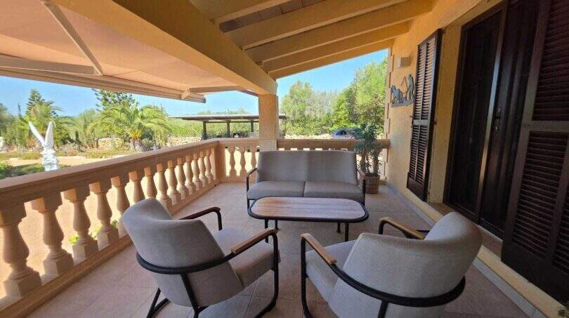 Überdachte Terrasse der Finca S'Illot mit grauer Lounge-Möbelgruppe und Blick auf mediterranen Garten
