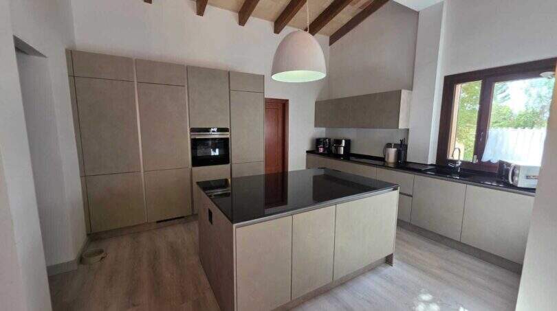 Moderne Einbauküche mit Kochinsel, schwarzer Granitarbeitsplatte und Holzbalkendecke in mallorquinischer Finca
