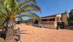 Finca S'Illot: Gepflasterter Innenhof mit Palmen, Steinbalustrade und mediteraner Fassade unter blauem Himmel.