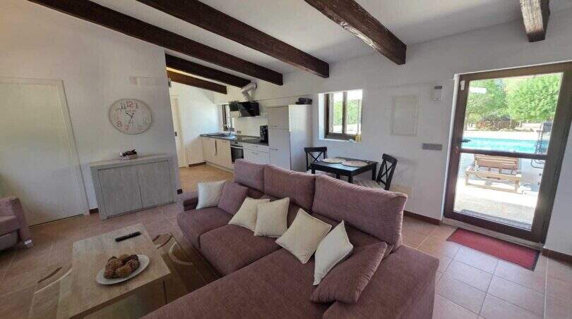 Helles Wohnzimmer mit Holzbalkendecke, Sofa, offener Küche und Poolblick der Finca in S'Illot