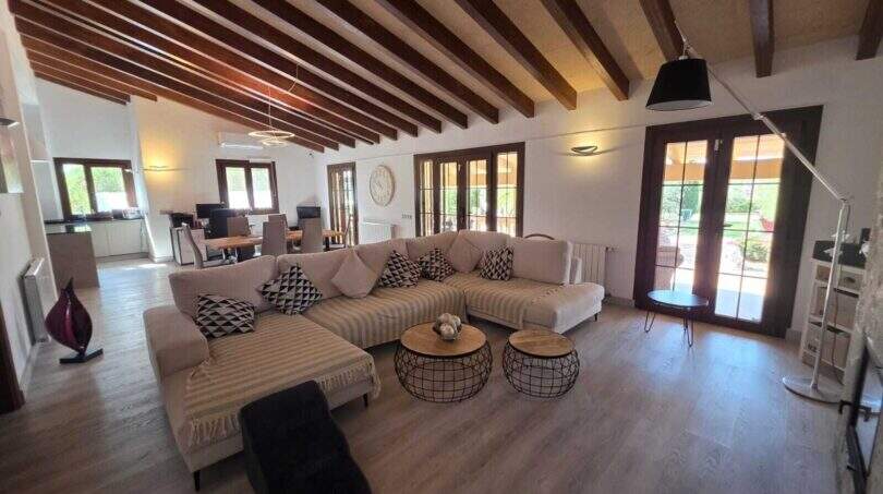 Helles Wohnzimmer der Finca S'Illot mit Holzbalkendecke, großem Ecksofa und Zugang zum Garten