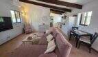 Helles Wohnzimmer der Finca S'Illot mit Holzbalkendecke, rosa Sofa, offener Küche und Klimaanlage