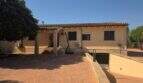 Außenansicht einer mallorquinischen Finca mit Ziegeldach, Einfahrt, Carport und üppigem Grün in S'Illot.
