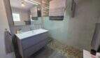 Modernes Badezimmer der Finca S'Illot mit Walk-in-Dusche, Kieselsteinboden und schwebenden Waschtisch in Grau.