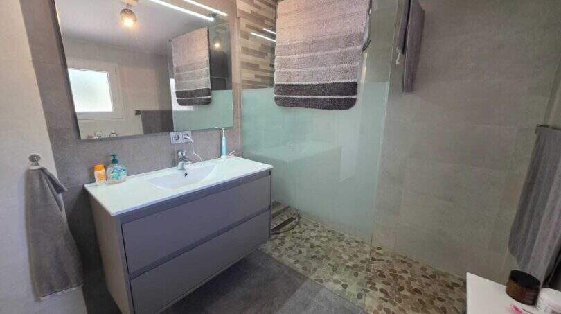 Modernes Badezimmer der Finca S'Illot mit Walk-in-Dusche, Kieselsteinboden und schwebenden Waschtisch in Grau.