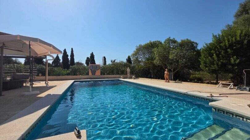 Großer Außenpool mit blauem Wasser, Sonnenschirm und mediterranem Garten der Finca in S'Illot