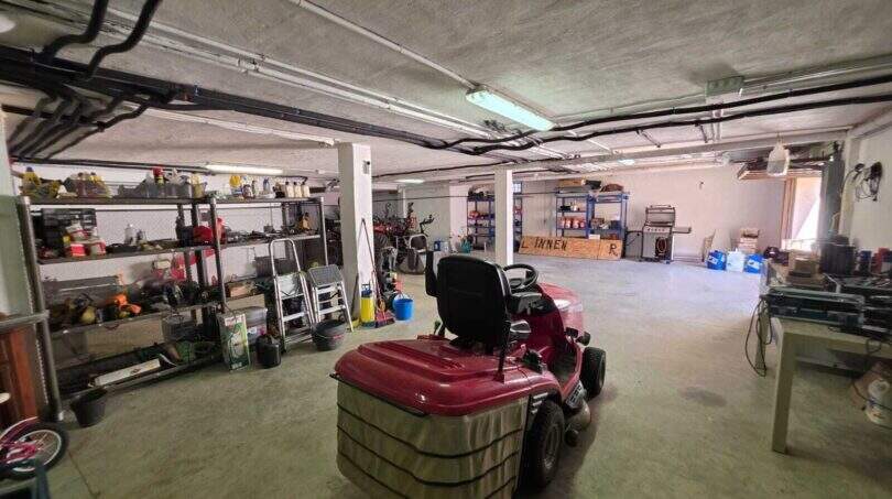 Geräumige Garage der Finca S'Illot mit Aufsitzrasenmäher, Werkzeugregalen und viel Stauraum.