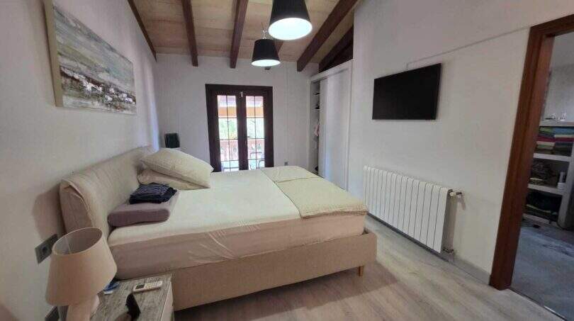 Helles Schlafzimmer der Finca S'Illot mit Holzbalkendecke, Doppelbett, TV und Balkonzugang
