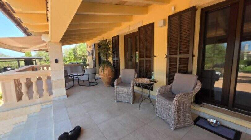 Überdachte Terrasse der Finca S'Illot mit Korbmöbeln, Holzläden und Hund auf Fliesenboden