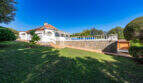 Außenansicht der weißen Poolvilla in Cala Murada mit Balustrade, Steinmauer und gepflegtem Garten.