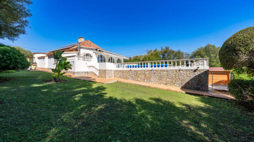 Außenansicht der weißen Poolvilla in Cala Murada mit Balustrade, Steinmauer und gepflegtem Garten.