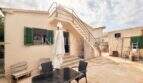 Terraza soleada con muebles de jardín, contraventanas verdes y escalera exterior de la casa mediterránea en Sa Ràpita
