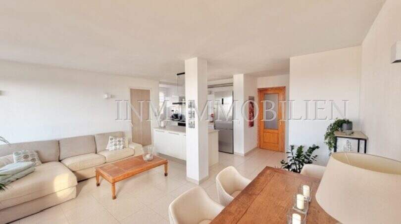 Heller Wohn-Essbereich mit Sofa, Holztisch, offener Küche und Terrakottaboden in Palmanova-Wohnung.