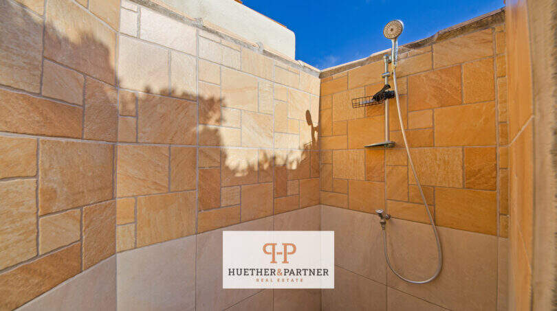 Outdoor-Dusche mit Naturstein-Wandverkleidung und Handbrause unter blauem Himmel, Cala Murada Haus mit Pool