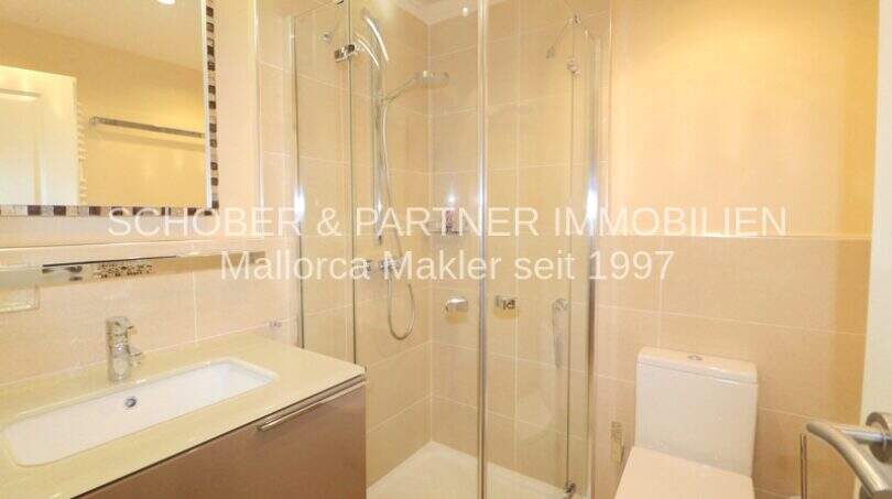 Baño moderno del apartamento de 4 habitaciones en Cala Millor con ducha de cristal, inodoro y lavabo luminoso.
